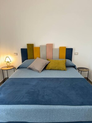 A bed with a blue bedspread and pillows in various colors, a bedside lamp, and a wall-mounted light fixture. - Suite Apartment Dora - Private access to the sea (Riposto)