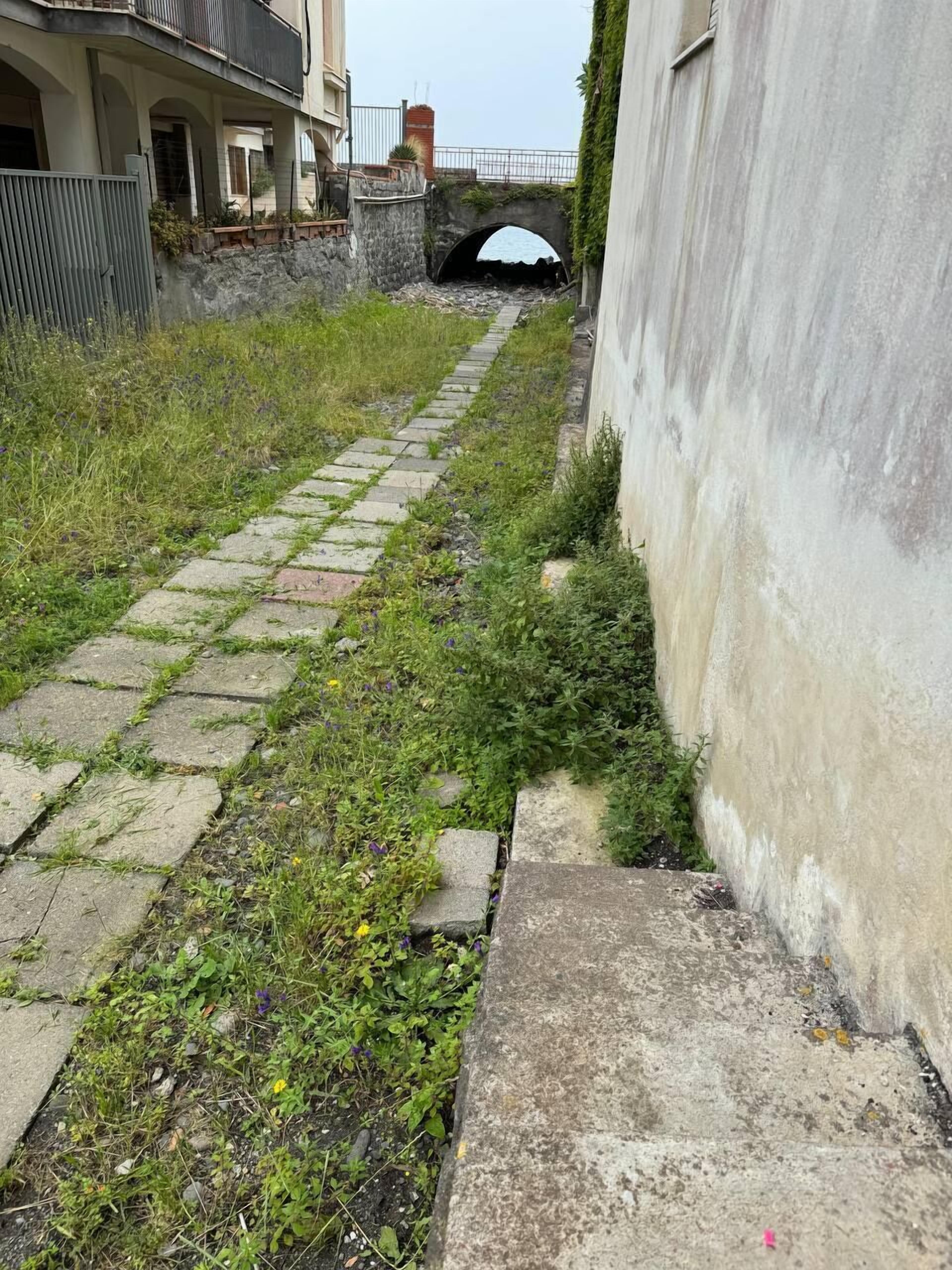 Ein schmaler Gang mit einem Steinweg, einem kleinen Bogen und einem Gebäude mit weißer Fassade.