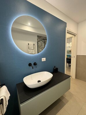 A bathroom with a large oval mirror, a white sink, and a black countertop. - Suite Apartment Dora - Private access to the sea (Riposto)