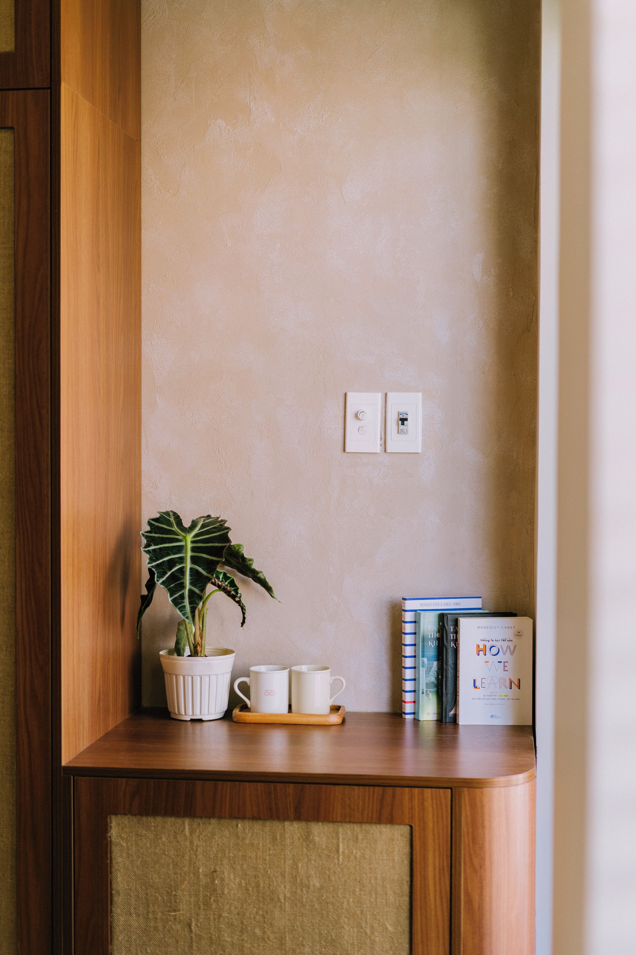 A wooden cabinet with a potted plant, two white mugs, and a tray with books.