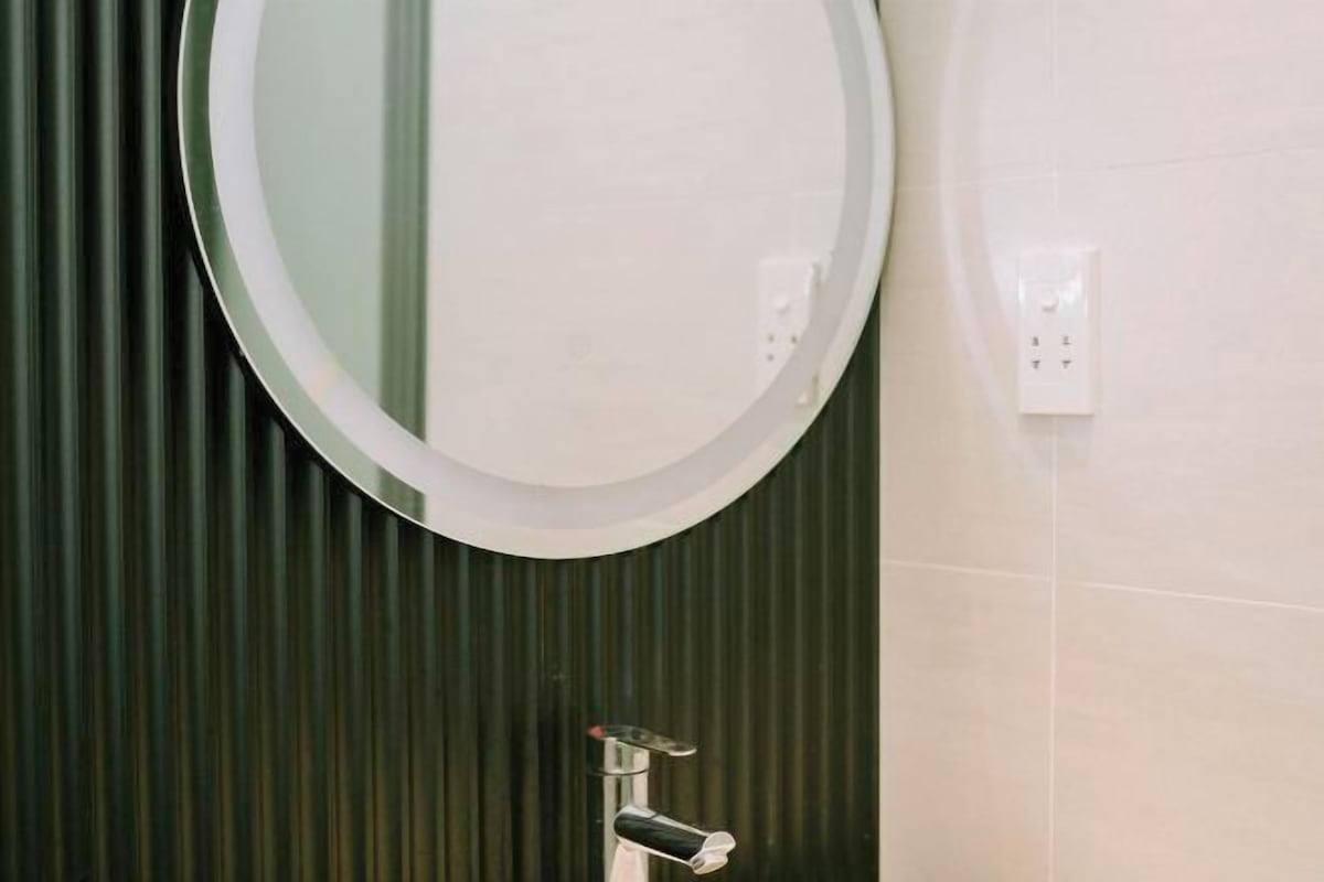 A bathroom with a round mirror, a faucet, and a light switch on the wall.