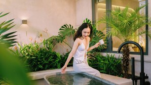 A woman in a white dress sitting by a small pool surrounded by lush greenery.