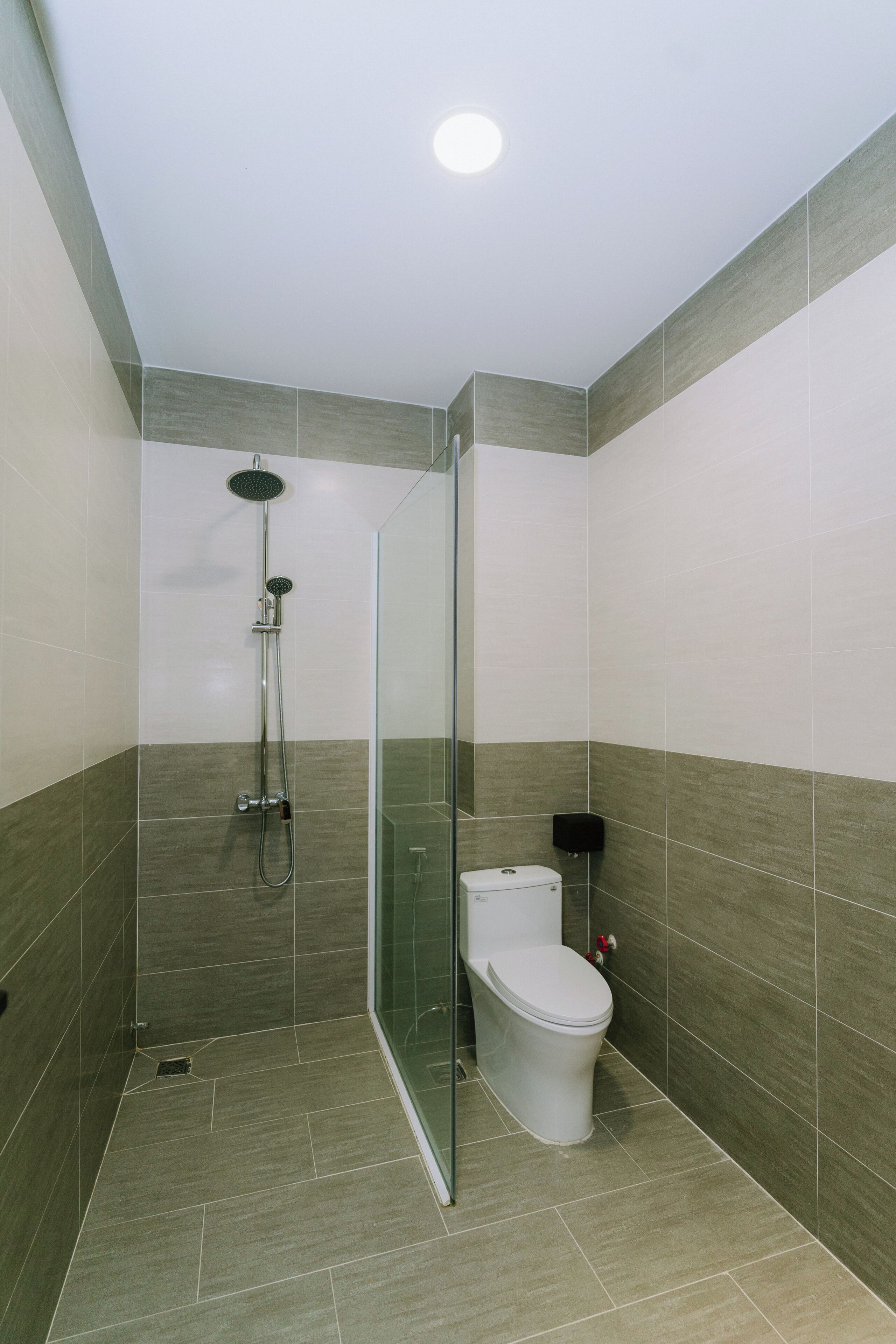 A modern bathroom with a glass shower enclosure, a toilet, and a hand dryer.