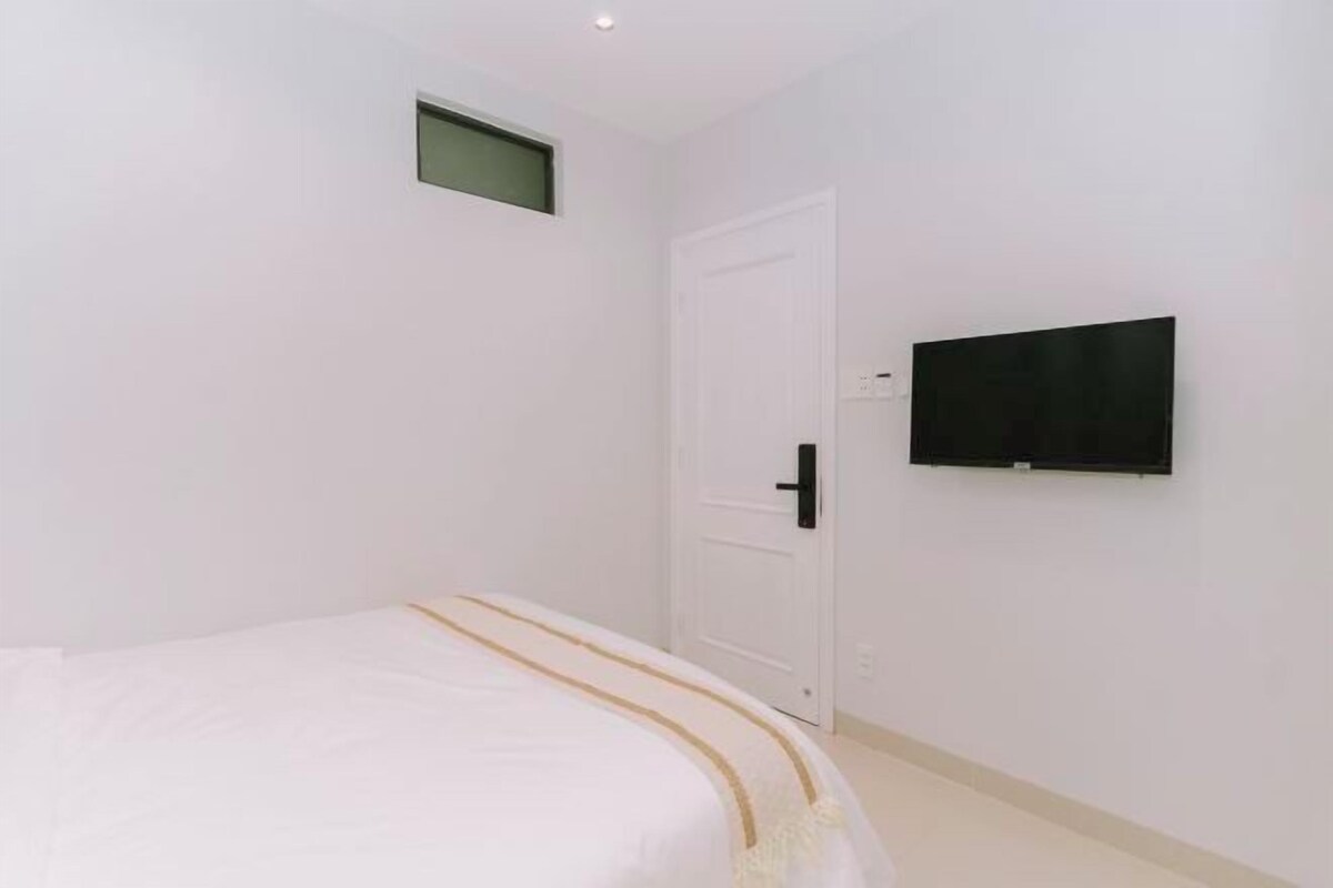 Une chambre à coucher avec un lit, une porte, un téléviseur fixé au mur et une petite fenêtre.