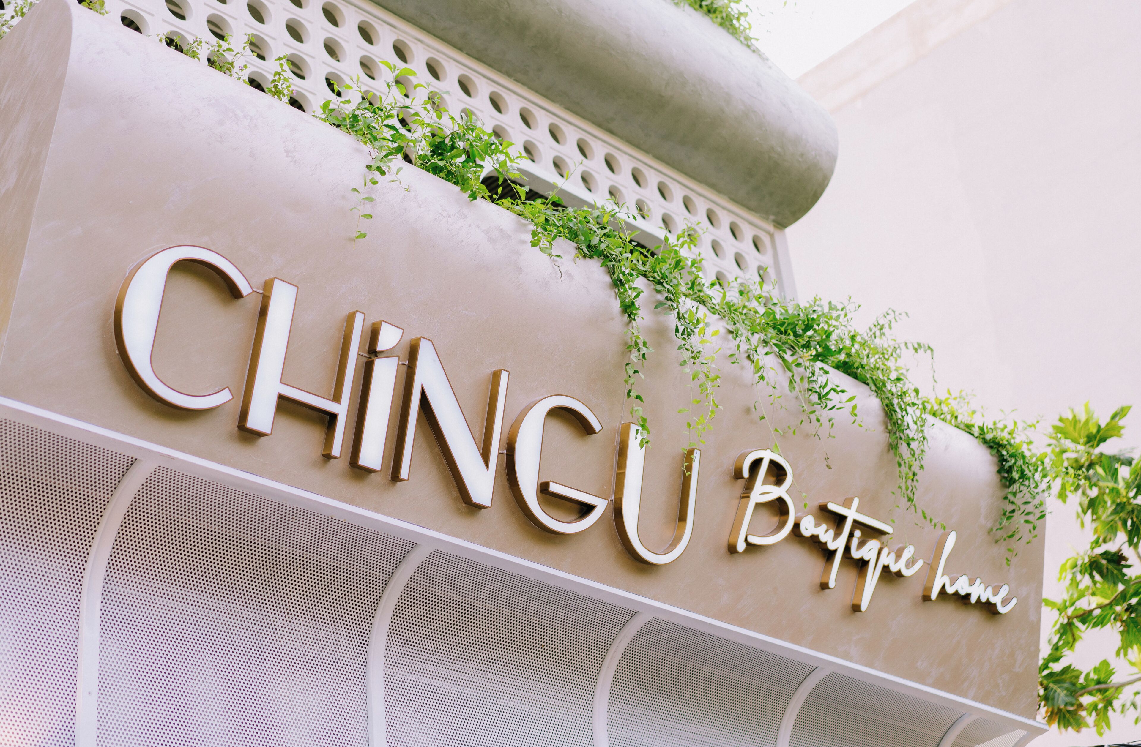 A sign for CHINGU Boutique home with a modern design and greenery.