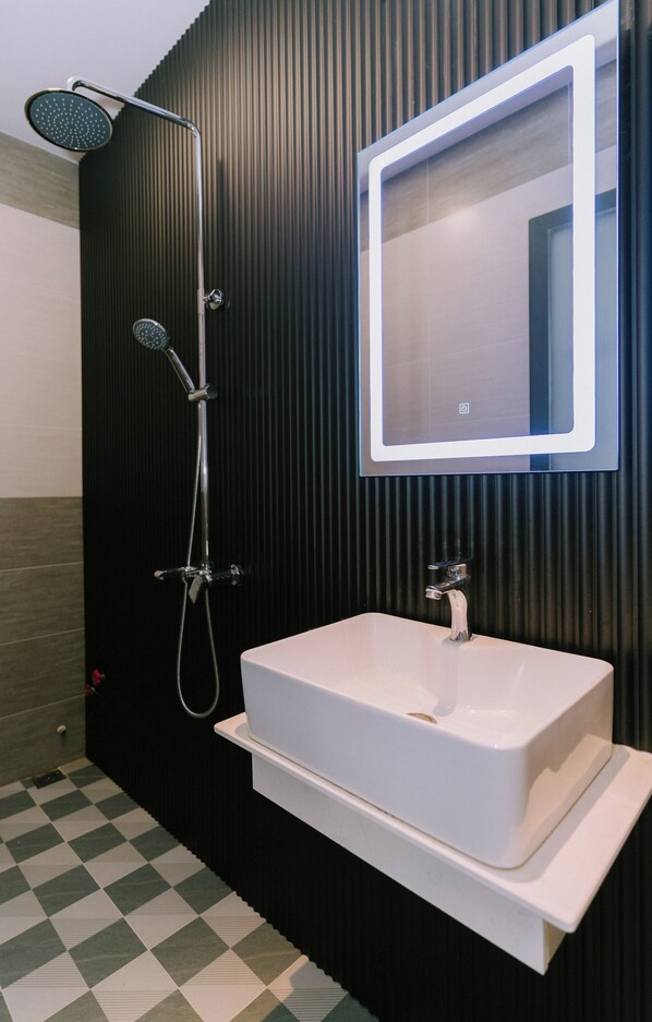 Une salle de bain moderne avec un lavabo blanc, une douche équipée d’un pommeau de douche à main et un miroir avec éclairage intégré.