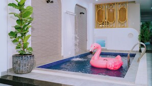 A swimming pool with a pink flamingo float, a potted plant, and a tiled wall with a decorative panel.