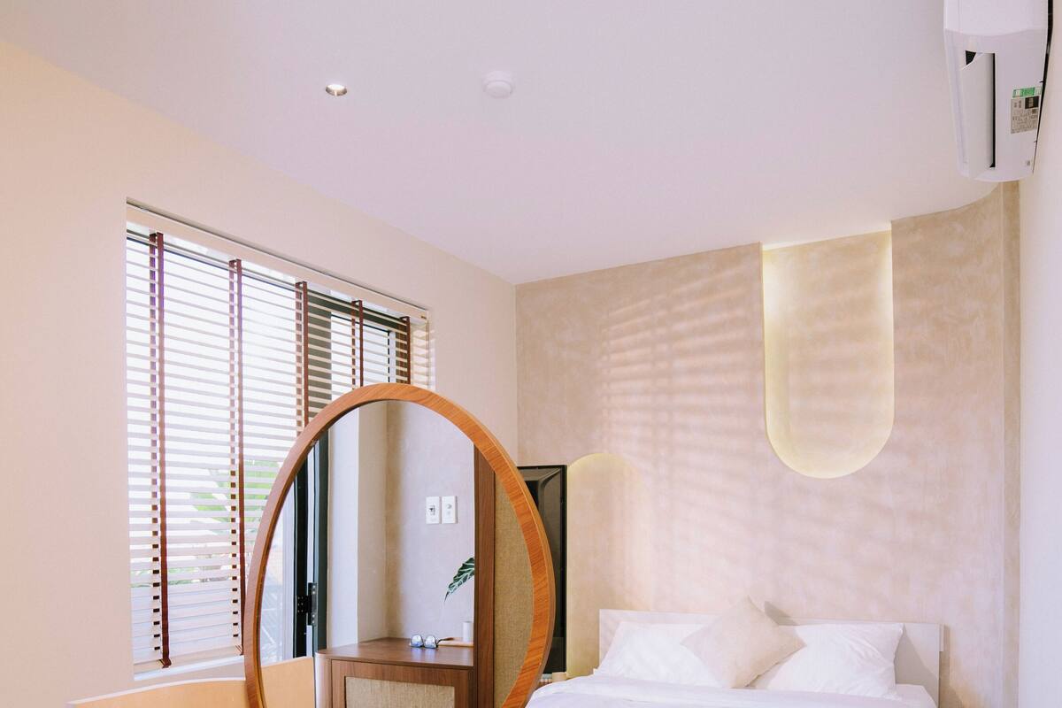 Un dormitorio con una cama, un escritorio con silla, un espejo y una ventana con persianas.