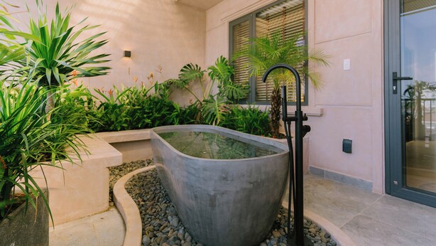 A modern bathroom with a large, curved bathtub, surrounded by lush greenery and a stone planter.