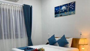 A neatly arranged bedroom with a wooden bed, blue bedding, a bedside lamp, and a night sky artwork on the wall. - Ha Anh Phan Thiet Hotel (Phu Thuy)