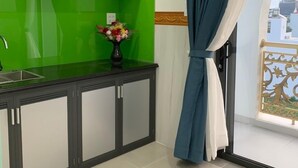 A modern kitchen with a green backsplash, a black countertop, and a cabinet with glass doors. There is a vase with flowers on the countertop. - Ha Anh Phan Thiet Hotel (Phu Thuy)