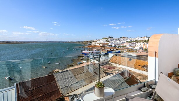 A coastal town with boats docked along the shore, a clear blue sky, and a view of buildings and a bridge in the distance.