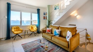 A living room with a sofa, two armchairs, a coffee table, and a view of the sea through large windows.