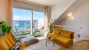 A modern living room with a yellow sofa, a coffee table, and a view of the sea through large windows.
