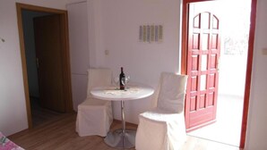 A small room with a round table, two chairs, a bottle of wine, and a red door. - Apartment Antonio (Bilice)