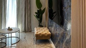 A modern living room with a marble floor, a round glass coffee table, a tufted ottoman, a large potted plant, and a flat-screen TV mounted on a marble wall. - Apartment Ivan With Pool (Zagvozd)
