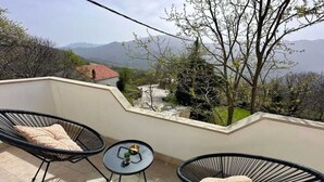 A balcony with two black wicker chairs, a small round table with a plant and a bowl, and a view of distant mountains and trees. - Apartment Ivan With Pool (Zagvozd)