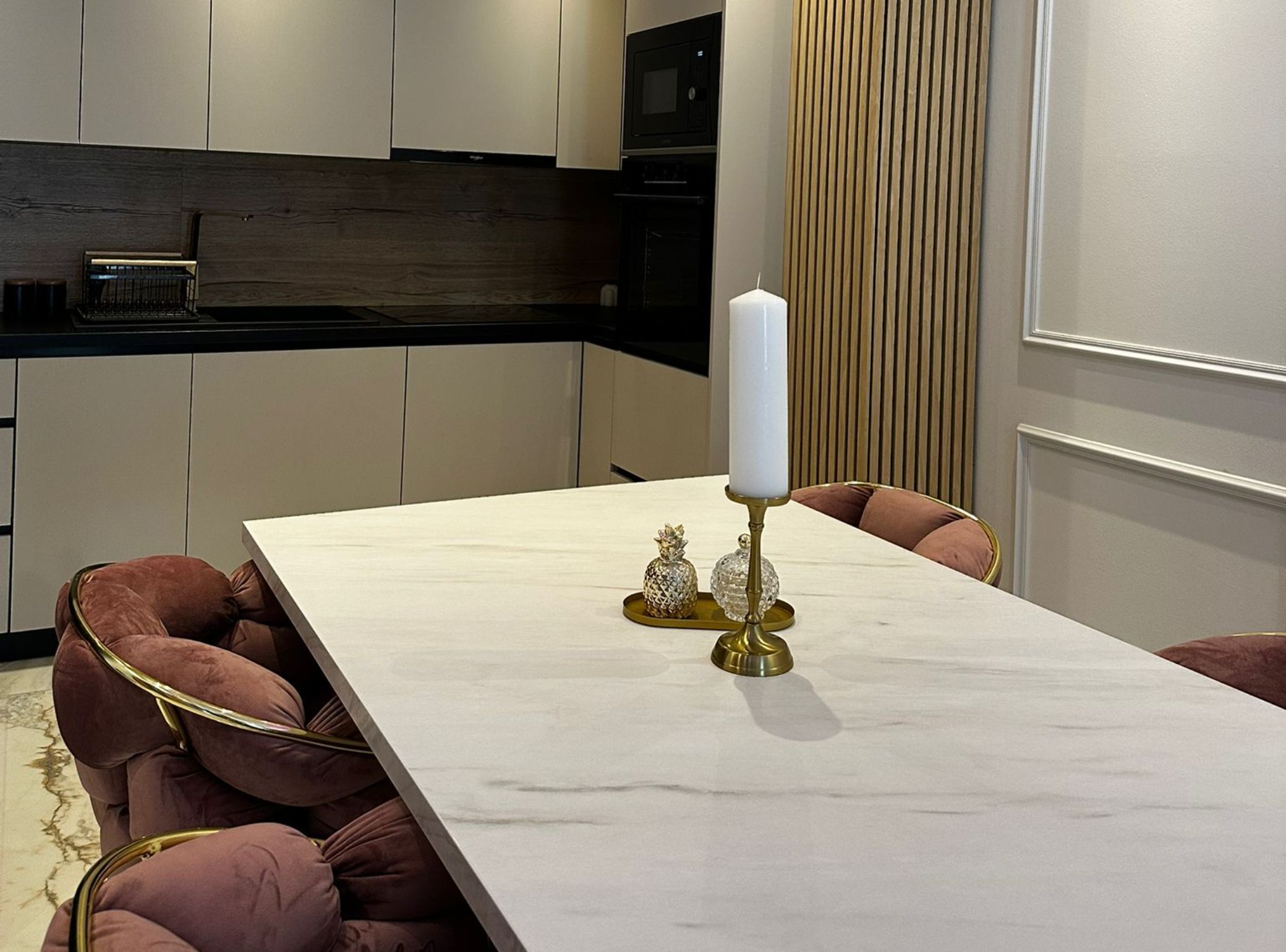 A modern dining area with a marble table, two chairs with gold accents, and a decorative candle holder.