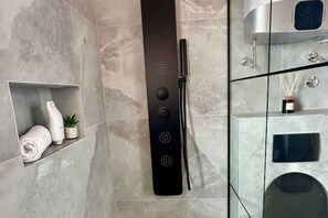 Un baño moderno con un panel de ducha negro, un inodoro con cerramiento de vidrio y un revestimiento de mármol.