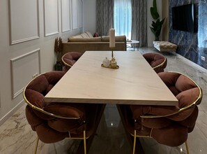 Un comedor moderno con una mesa de mármol, sillas tapizadas y un televisor al fondo.