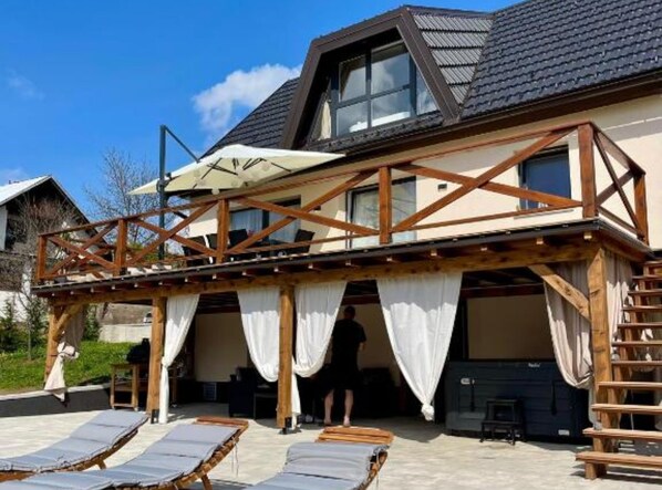 Ein zweistöckiges Gebäude mit einem Balkon und einer überdachten Sitzgelegenheit mit Liegestühlen.