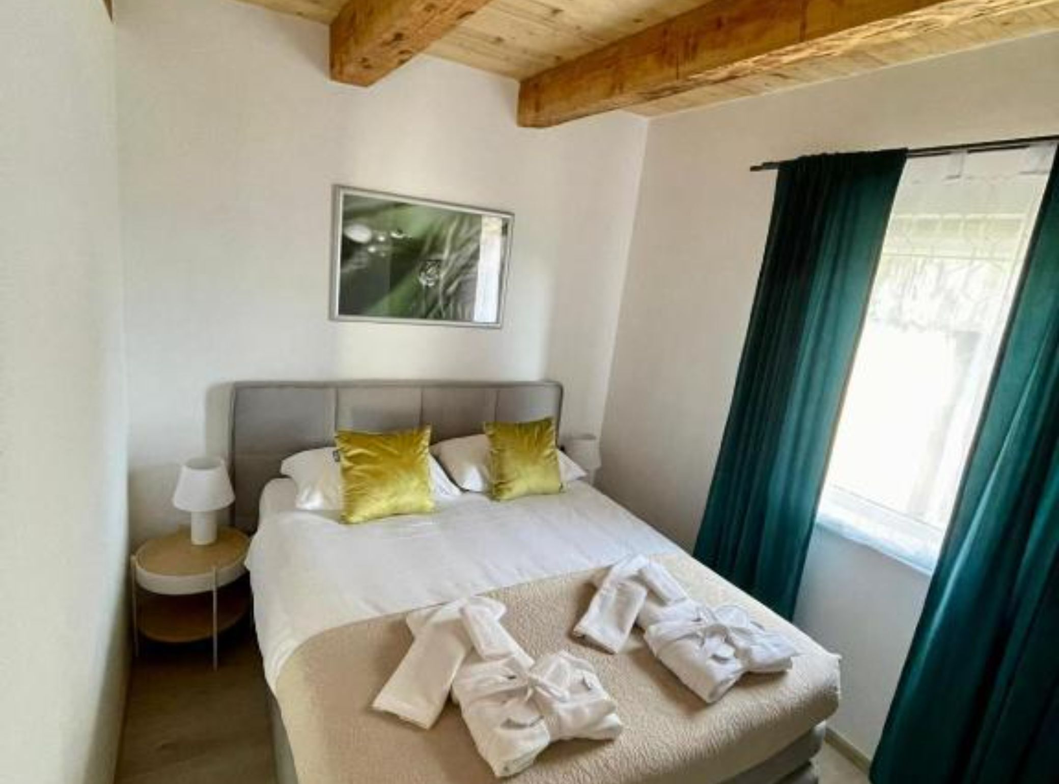 Ein Hotelzimmer mit Bett, Nachttisch, Lampe, einem Bild an der Wand und einem Fenster mit Vorhängen.