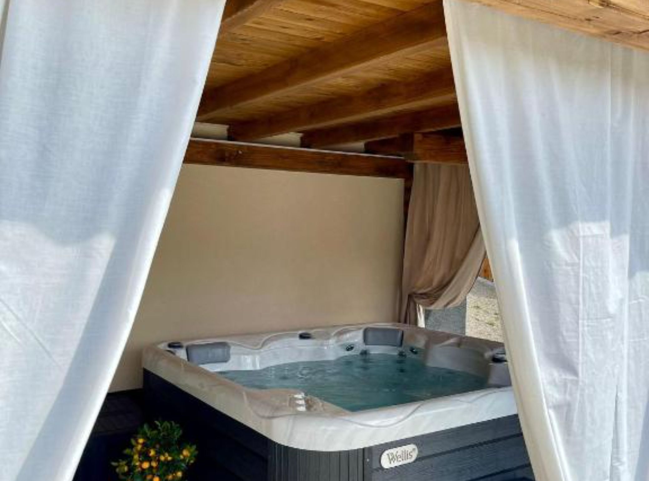 A hot tub under a wooden pergola with white curtains.