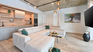 Et moderne køkken med indbygget ovn, et spiseområde med en lysegrå sofa og et stort billede på væggen.