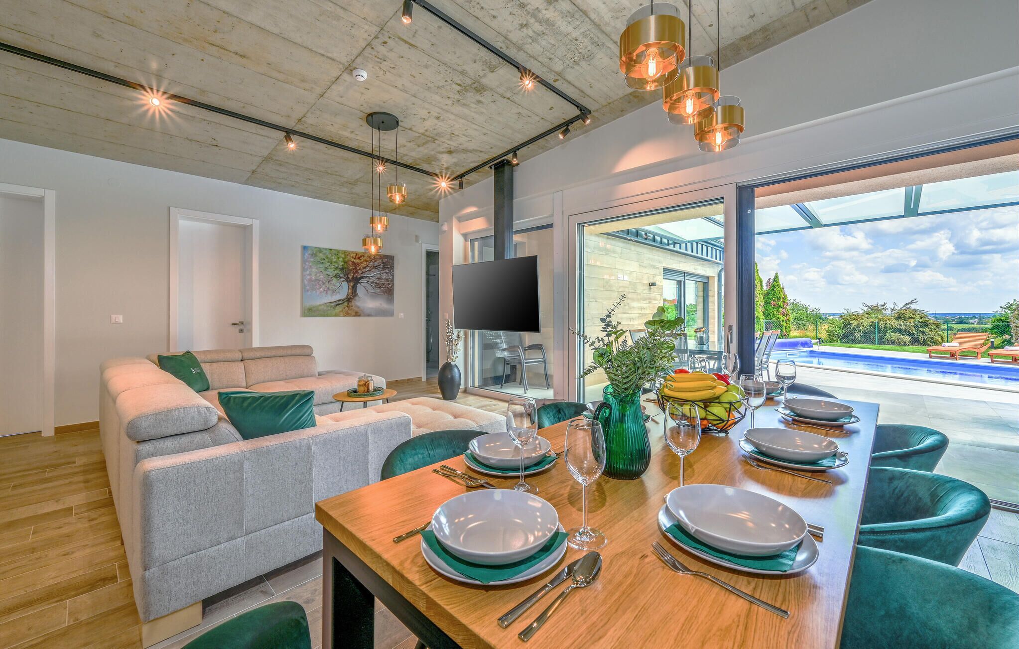 Een moderne eethoek met een houten tafel voor vier personen, een bank en een televisie op de achtergrond.
