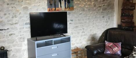 A living room with a stone wall, a flat-screen TV, a grey cabinet, a leather sofa, and a coffee table with decorative items.