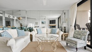 Un salon moderne avec un canapé blanc, une table basse en verre et un fauteuil à motifs.