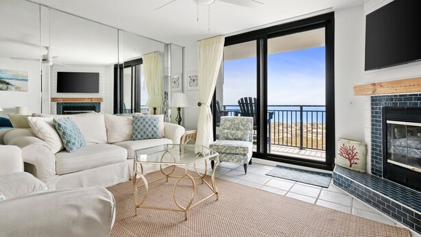 Un salon moderne avec un canapé, une table basse et une cheminée. Il y a un balcon avec vue sur l’océan.