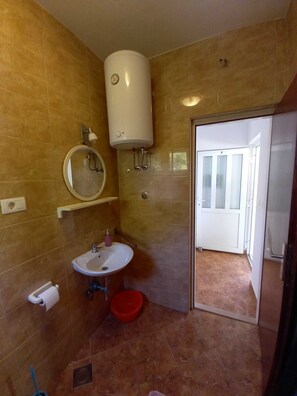Une salle de bain équipée d’un WC, d’un lavabo, d’un miroir et d’un chauffe-eau blanc fixé au mur.