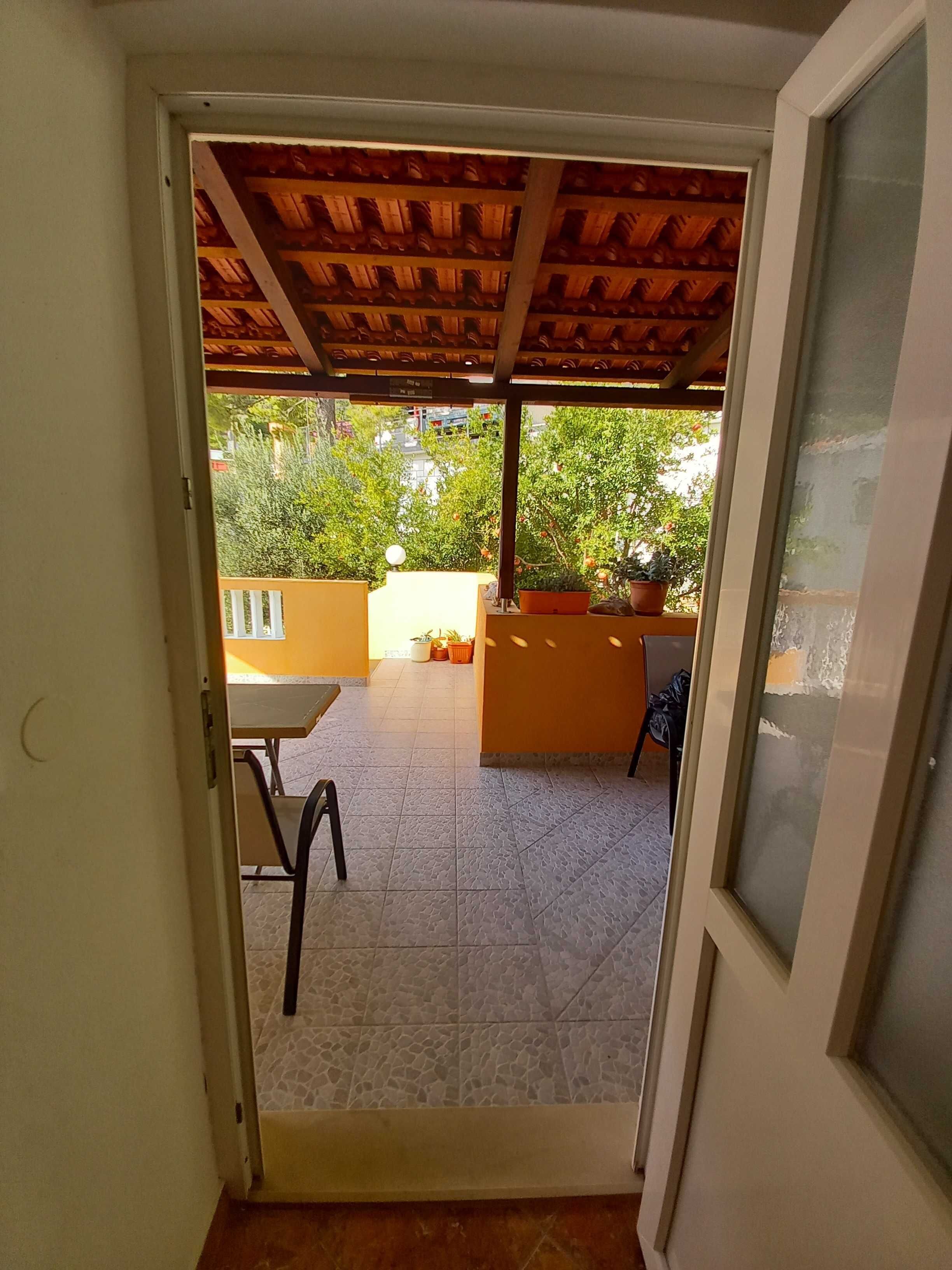 Une porte ouverte donnant sur un patio doté d’un sol carrelé, d’un plafond en bois et de mobilier d’extérieur.