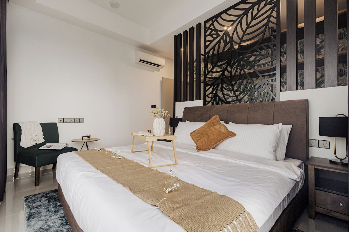 Une chambre d’hôtel moderne avec un grand lit, une table de chevet, une chaise et un panneau décoratif au mur.