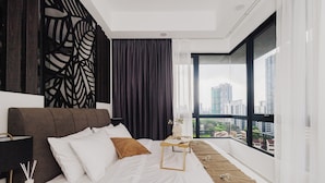 Une chambre d’hôtel moderne dotée d’un grand lit, d’une table de chevet et offrant une vue sur la ville, ainsi qu’un panneau décoratif mural.