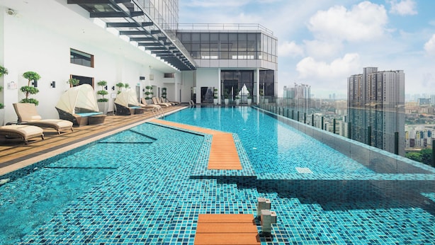 Une piscine à débordement située sur le toit, avec des chaises longues, une balustrade en verre et une vue sur la ville.
