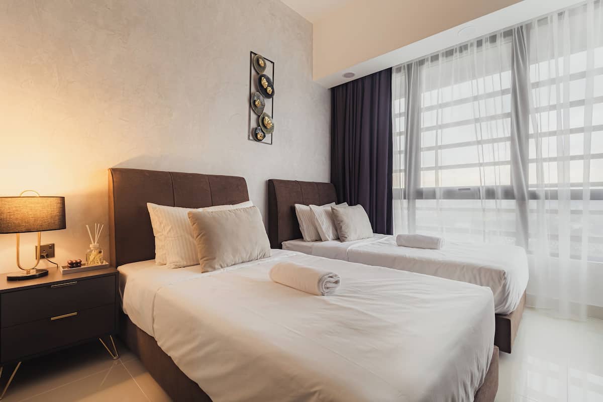 Une chambre d’hôtel avec deux lits, une table de chevet avec une lampe et une grande fenêtre avec des rideaux.