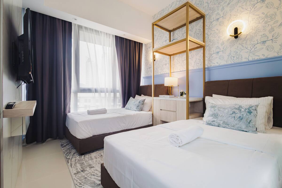 Une chambre d’hôtel avec deux lits, une télévision, un bureau avec une lampe et un grand miroir.