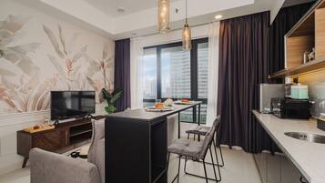 A modern kitchen with a dining area, a TV, and a large window with curtains.