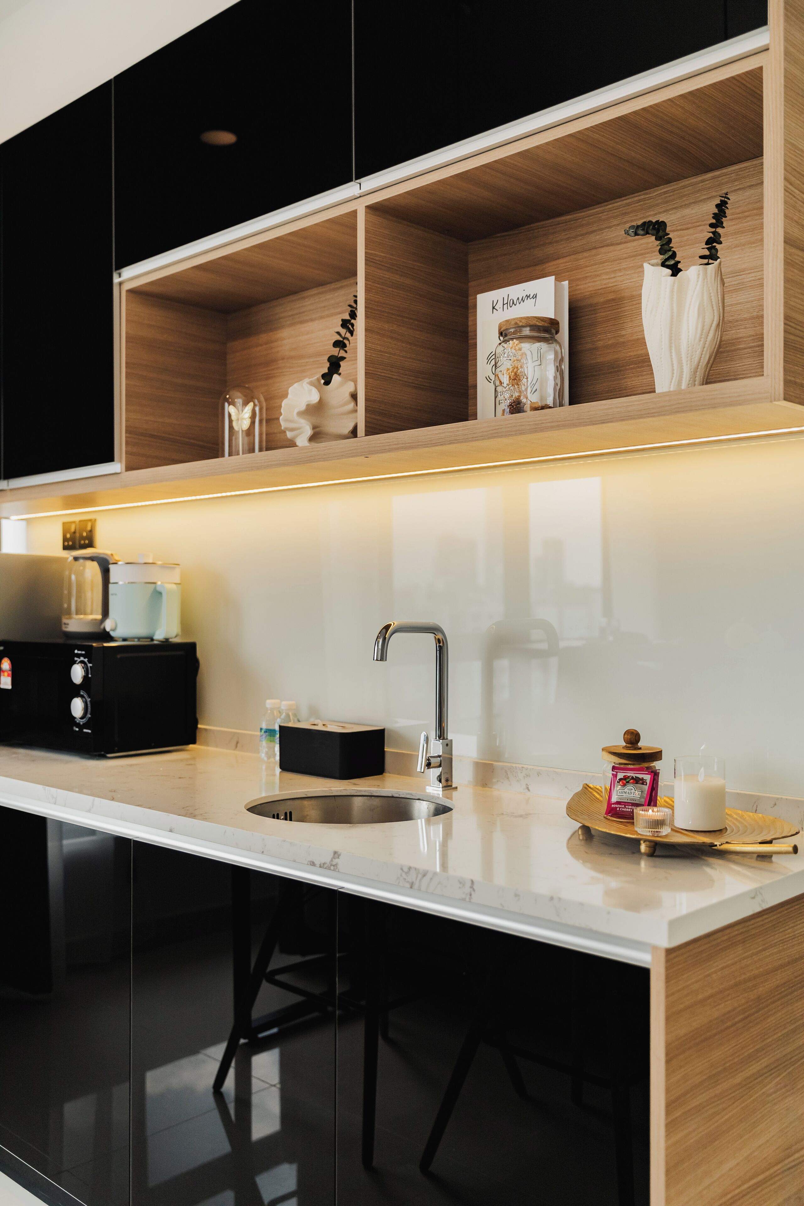 A modern kitchen with a built-in stove, a coffee machine, and a shelf with decorative items.