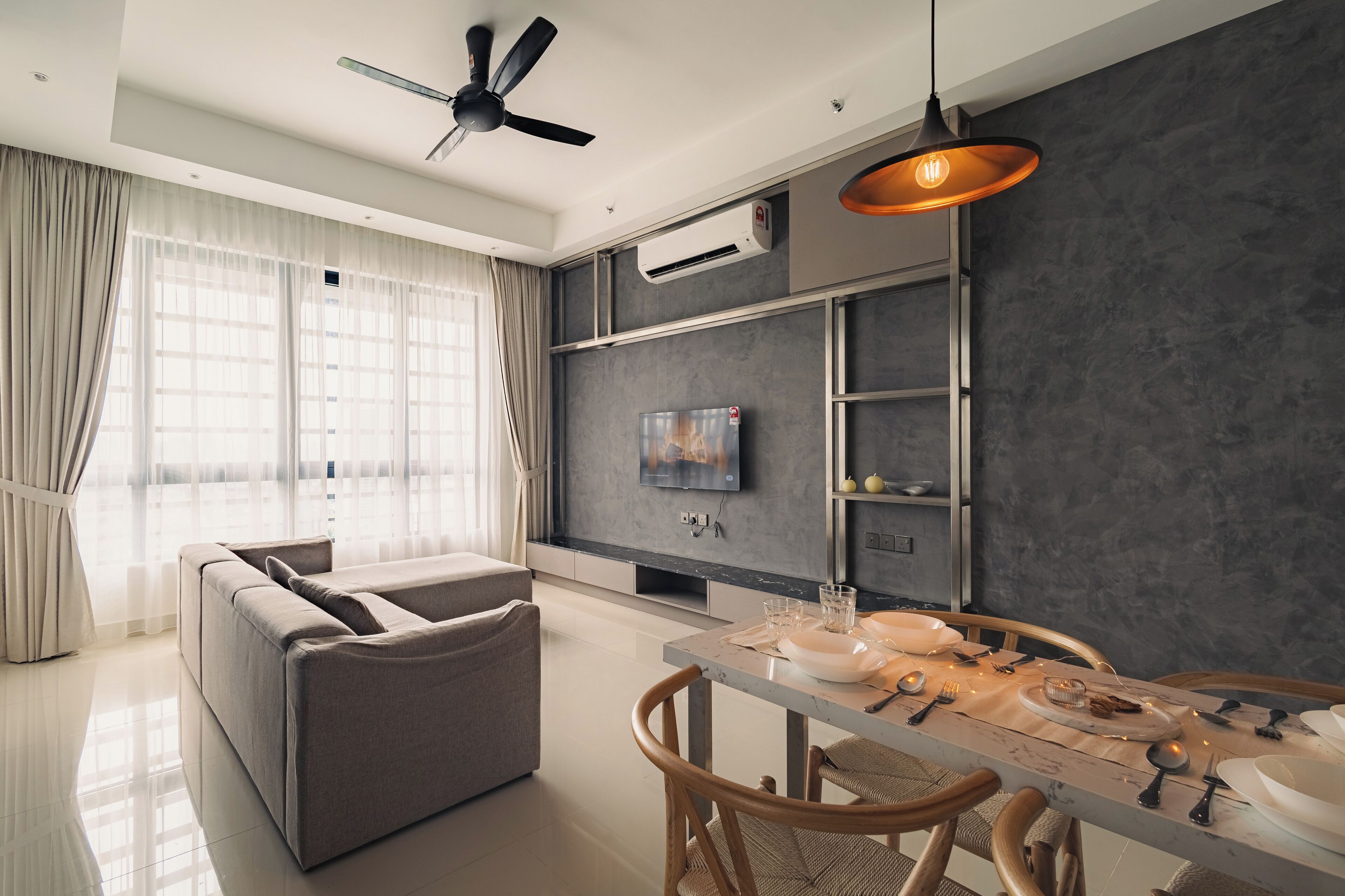 Un salon moderne avec un canapé, une table à manger et des chaises. On y trouve également un ventilateur de plafond, un appareil de climatisation et un téléviseur fixé au mur.