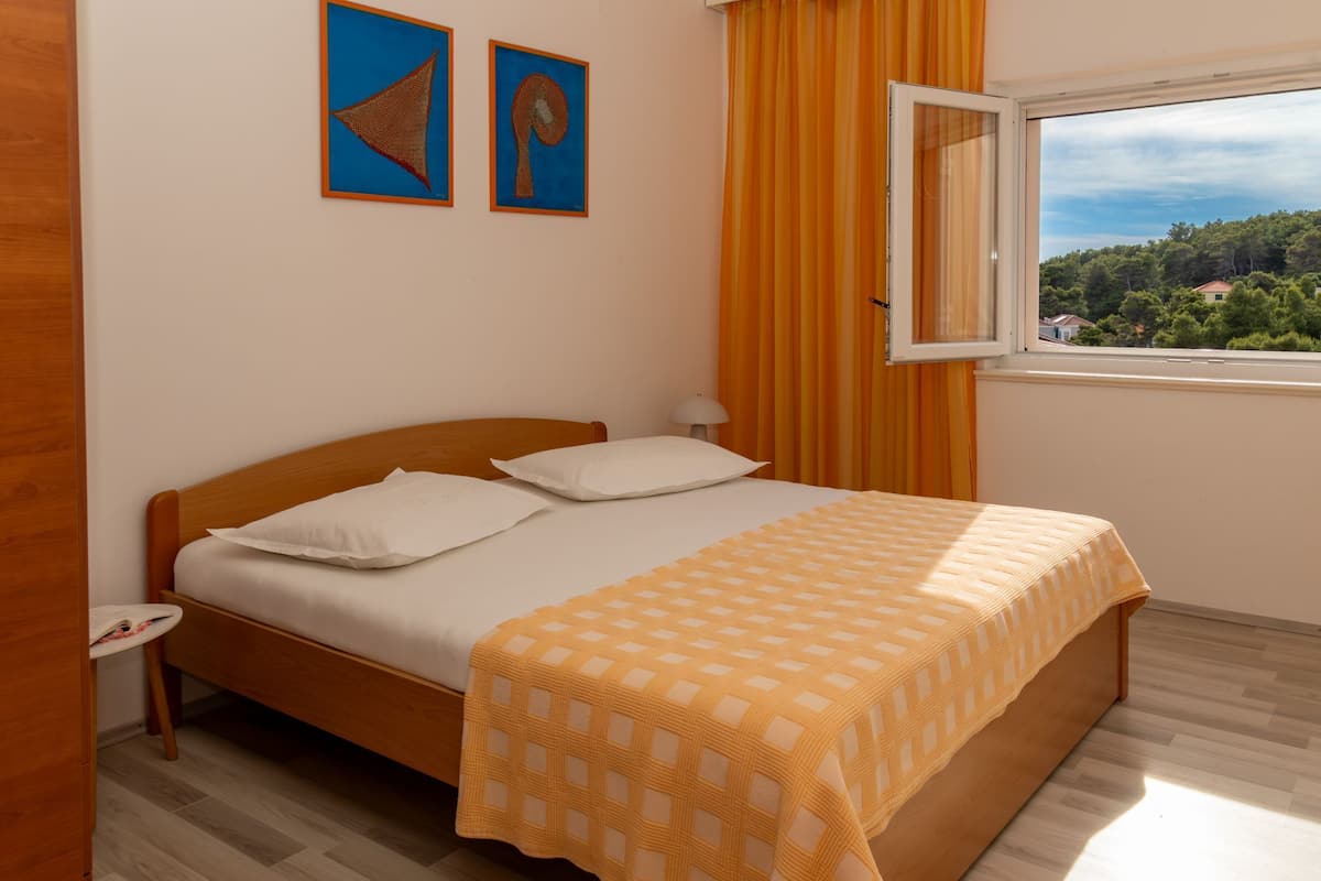 A bedroom with a wooden bed, white pillows, a yellow checkered blanket, and two framed artworks on the wall.