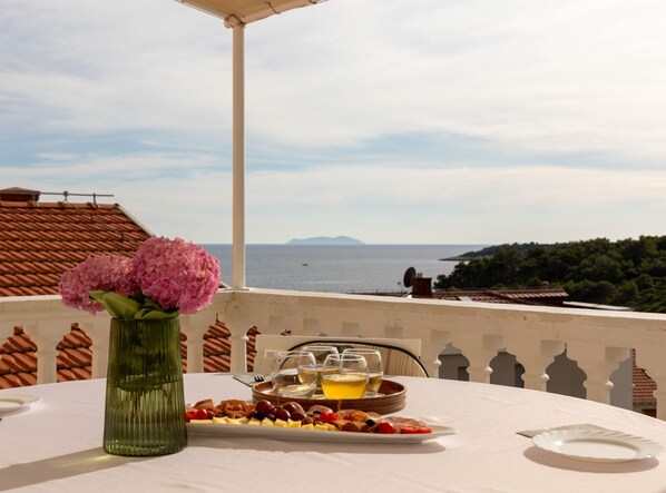 A table set with a fruit platter, glasses, and a bottle, overlooking a coastal view with a mountain in the distance. - Apartments Villa Marijana (Blato)