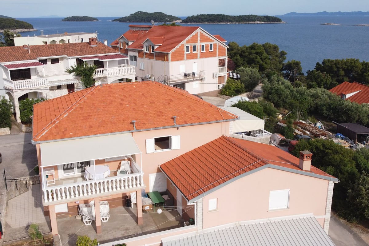 A two-story house with a red-tiled roof, a balcony, and a view of the sea.