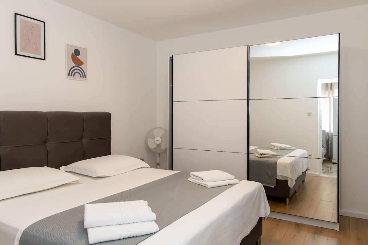 A modern bedroom with a large bed, a wardrobe, and a mirror.