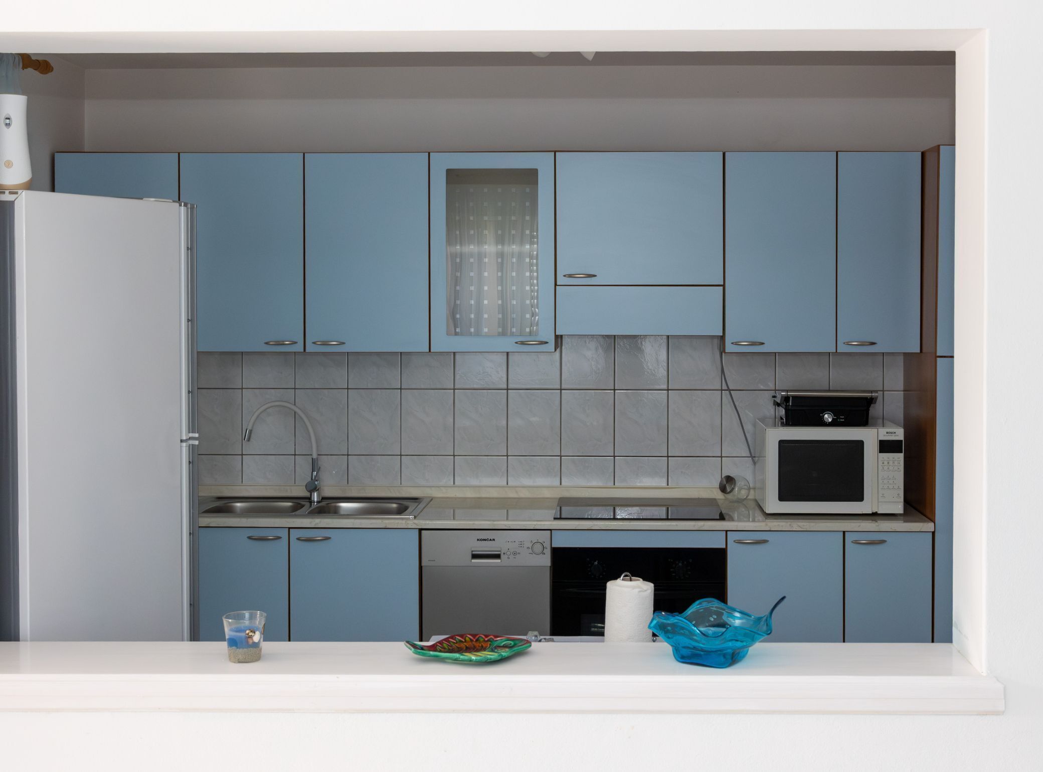 A compact kitchen with blue cabinets, a built-in microwave, and a dishwasher.