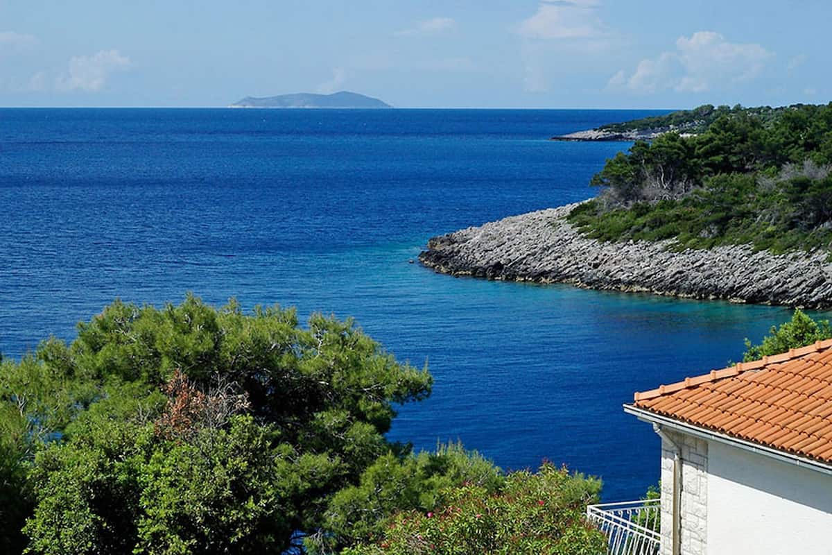 A coastal view with a clear blue sea, rocky shoreline, and greenery.