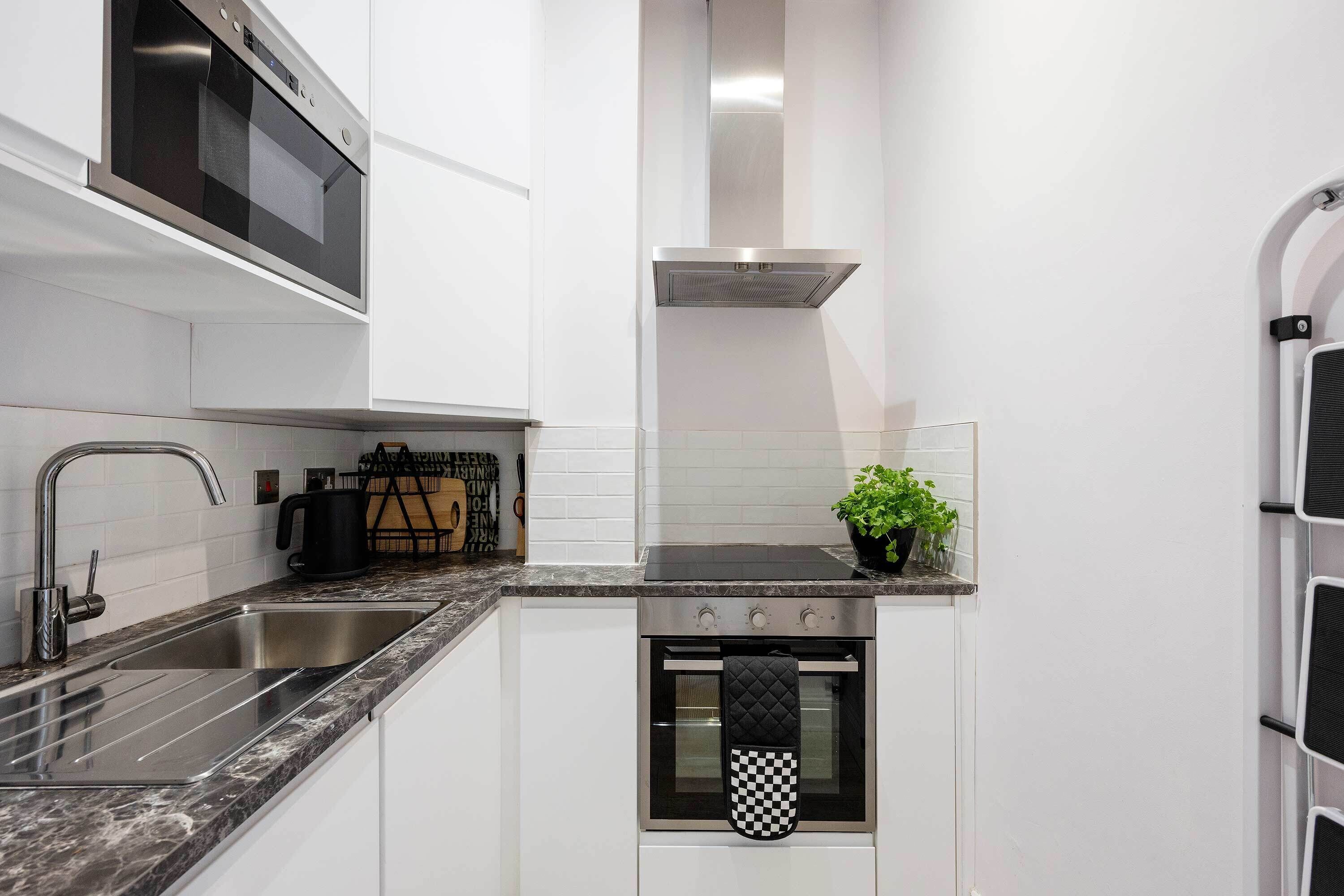 A modern kitchen with a stainless steel oven, a built-in microwave, and a black kettle on the countertop.