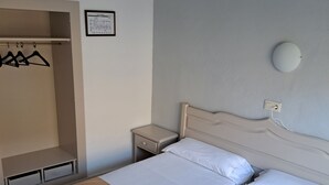 Habitación de hotel con dos camas, un armario, una mesita de noche y una lámpara de pared.